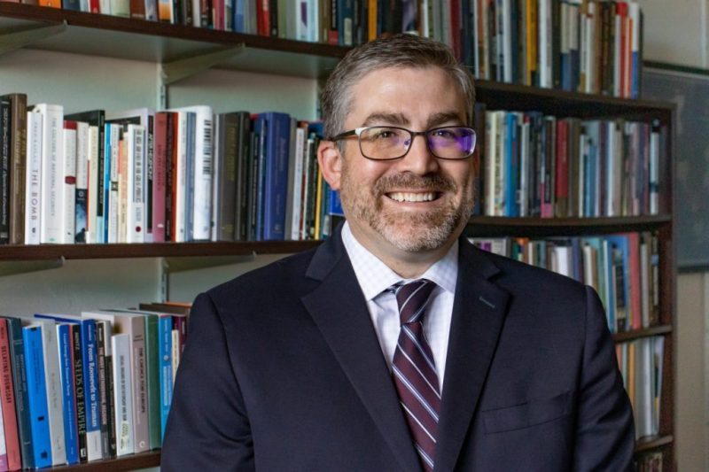 man in suit standing in front of book shelf